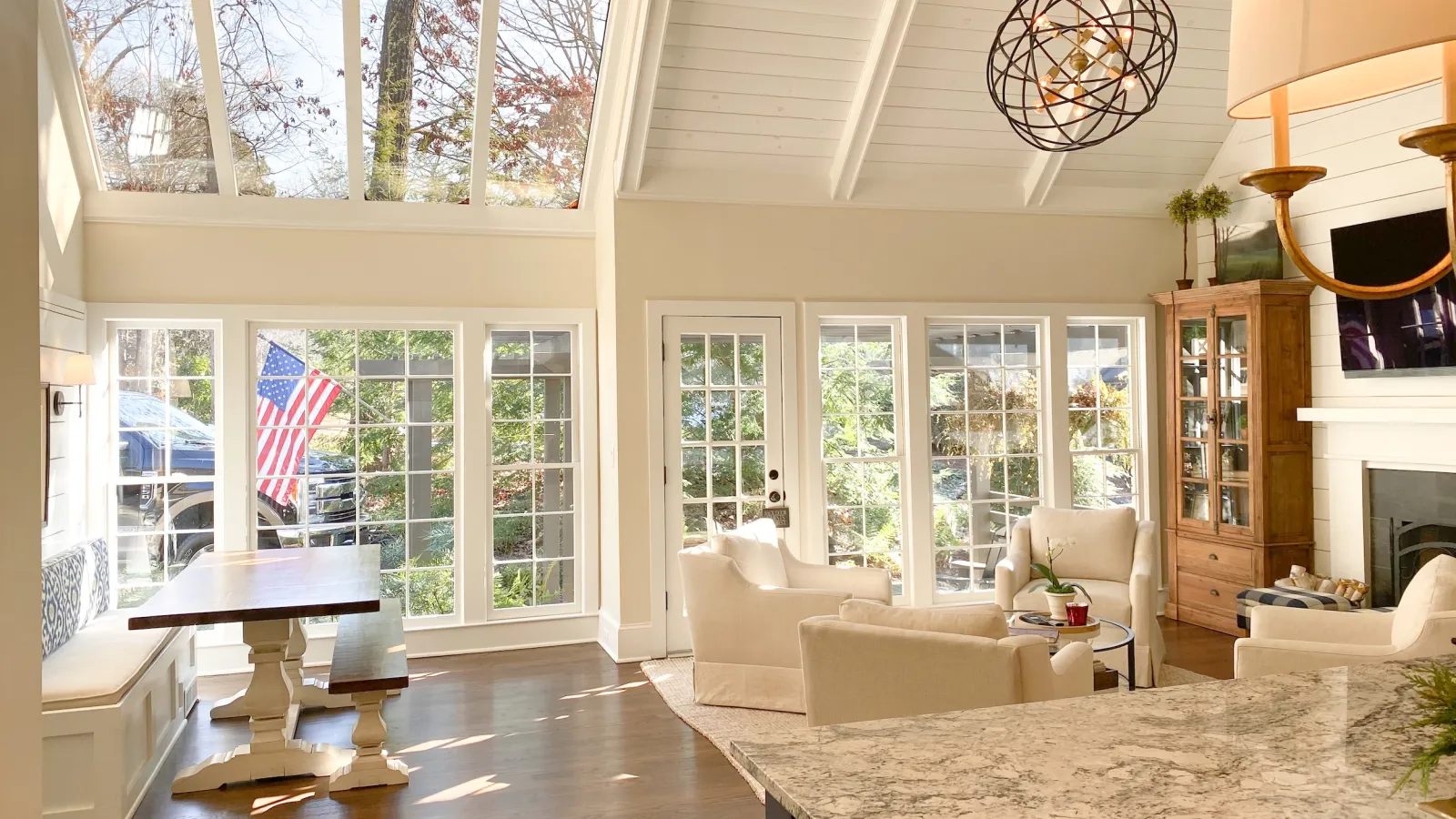 Bright open living room with large windows, skylights, white walls, beige furniture, hardwood floors, and modern chandelier
