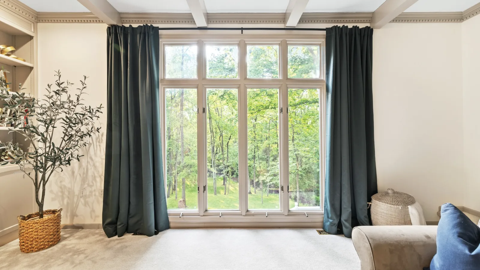 Large living room window with dark curtains overlooking green trees and beige interior furnishings.
