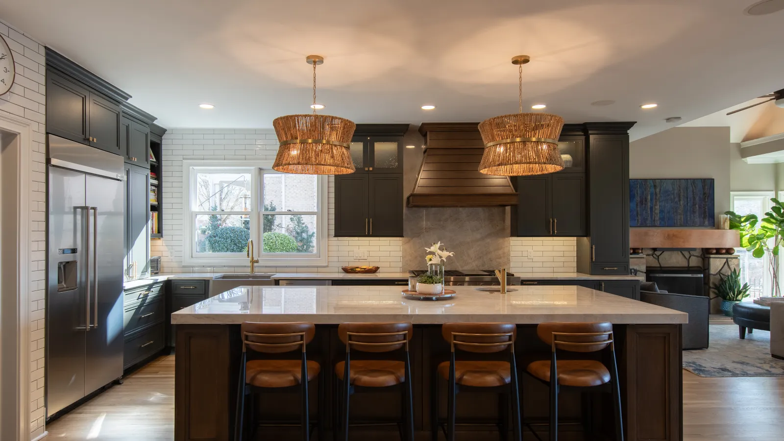 Modern kitchen with large island, brown bar stools, pendant lights, dark cabinetry, and stainless steel appliances.