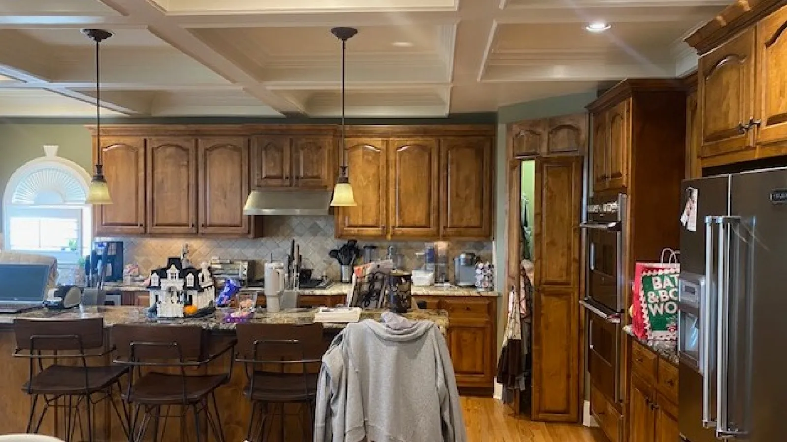 Cozy kitchen with wooden cabinets, granite countertops, three bar stools, stainless steel appliances, and overhead pendant lights