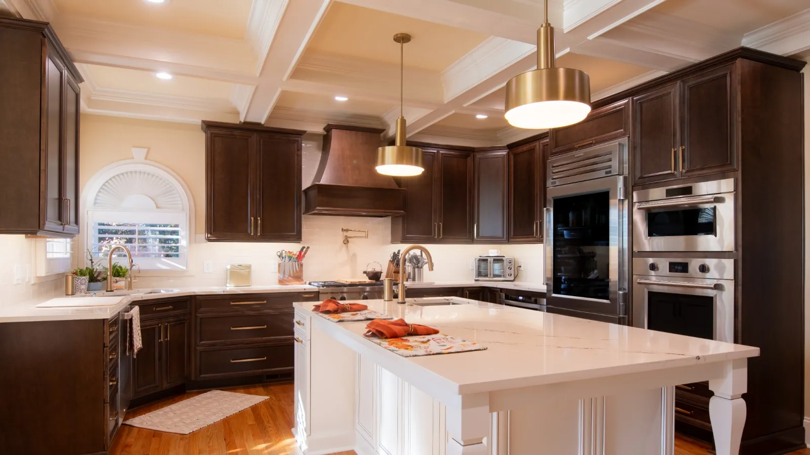 Modern kitchen with dark wood cabinets, white island, stainless steel appliances, and hardwood floors under coffered ceiling.