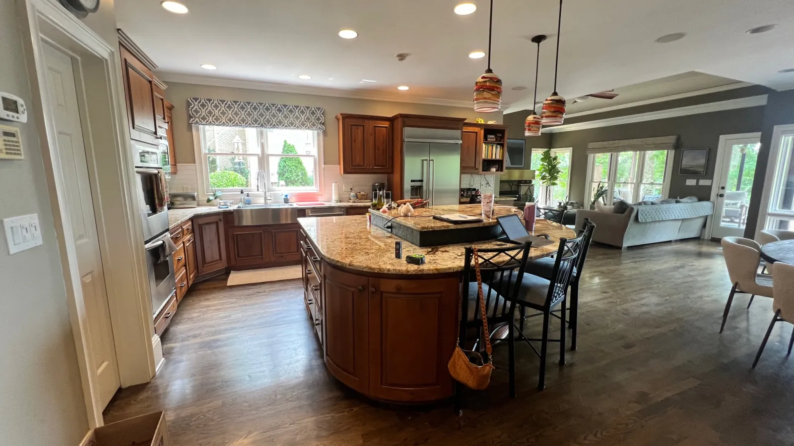 Spacious modern kitchen with wooden cabinets, granite island, stainless steel appliances, and open living area beyond.