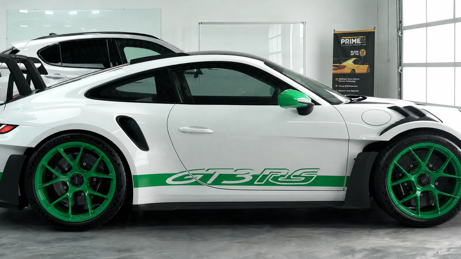 White Porsche GT3 RS sports car with green accents parked indoors with a black roof and green wheels.