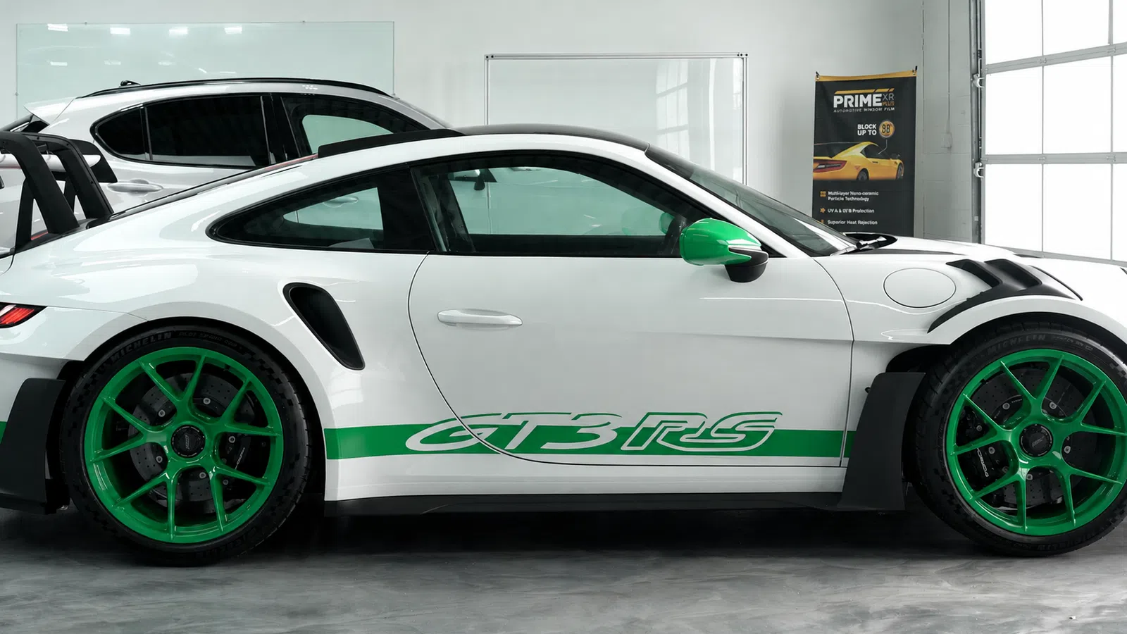Side view of a white Porsche GT3 RS with green accents and wheels in a showroom setting.