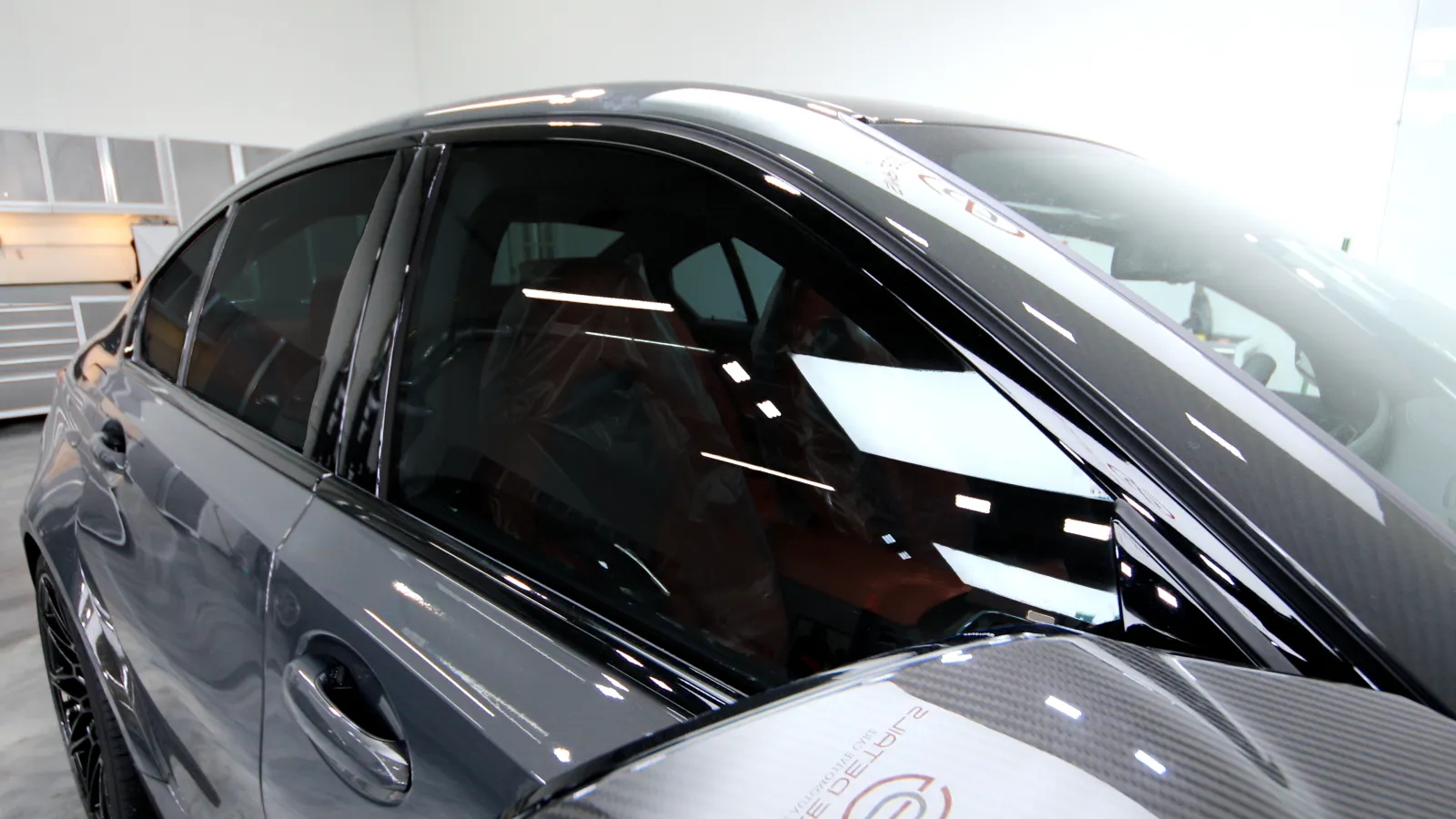 Close-up of a sleek black car with tinted windows and carbon fiber side mirror in a showroom.
