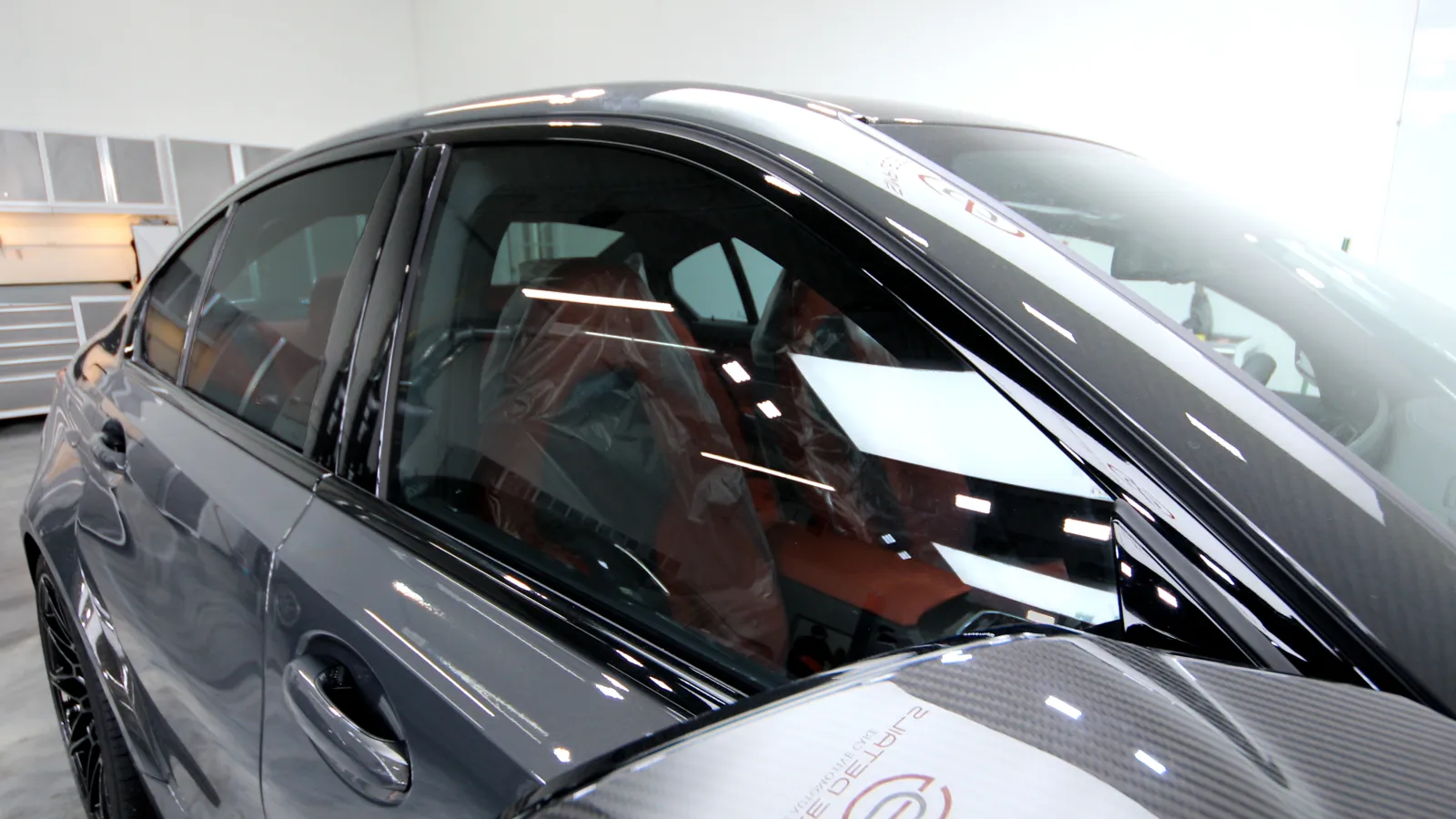Close-up of a shiny black luxury car's side window and door inside a bright garage.