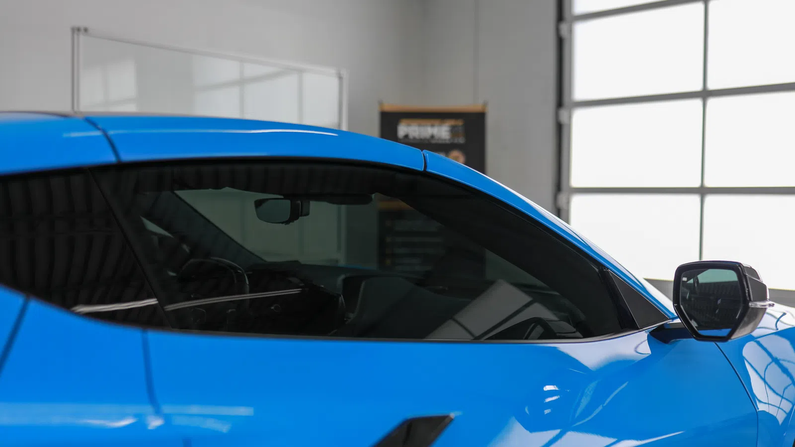 Close-up of a blue sports car side window and sleek side mirror in a bright garage setting