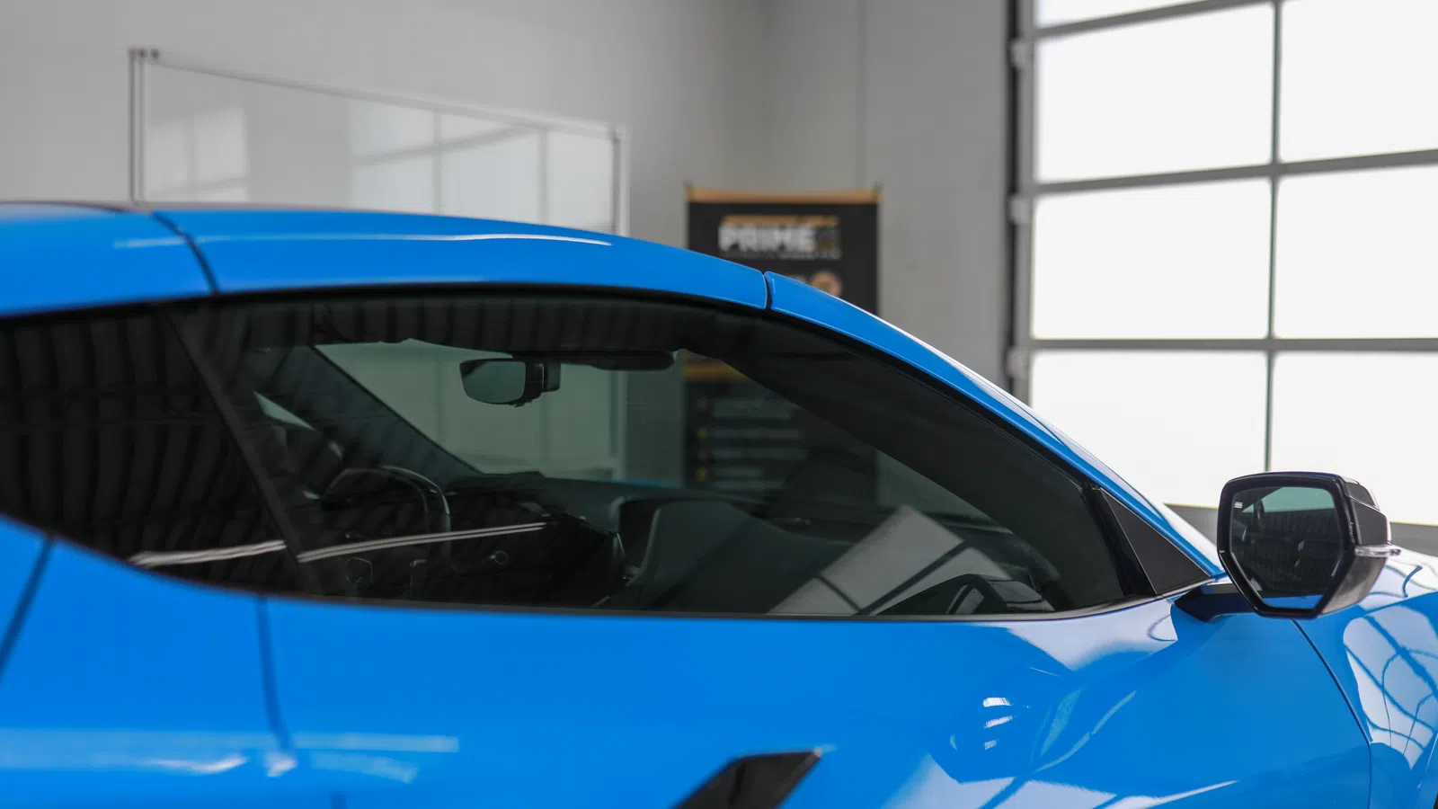 Side view of a sleek blue sports car focusing on the door, window, and side mirror inside a bright showroom.