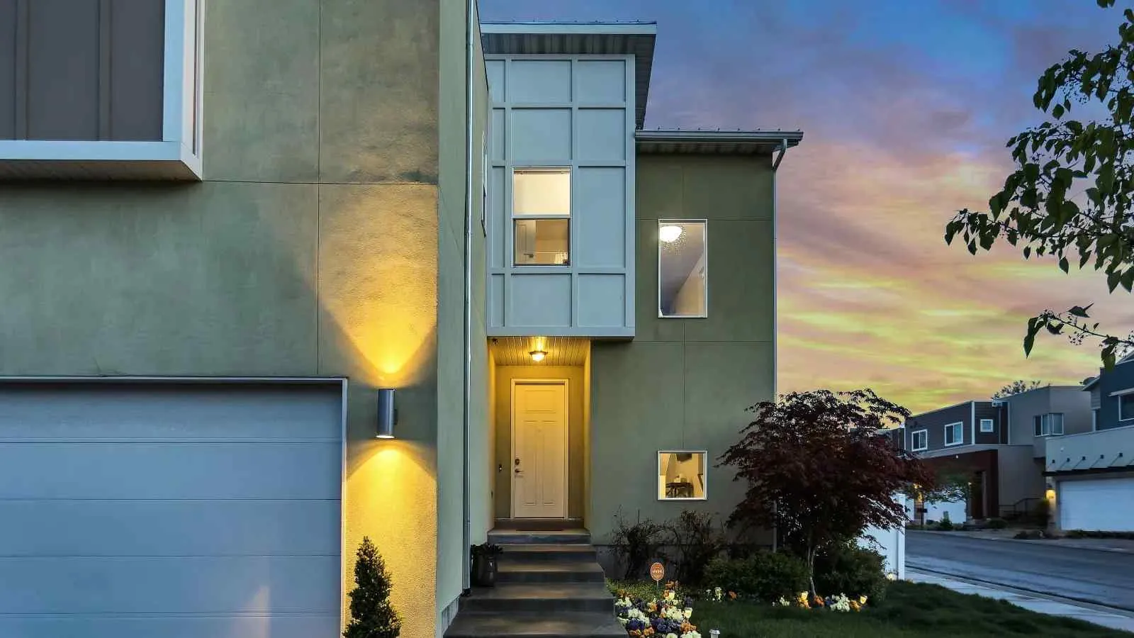Modern two-story house exterior with lit entrance and garage during colorful sunset sky.
