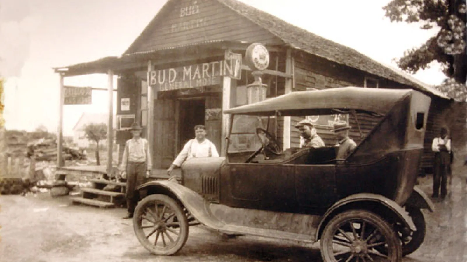 old picture of car and men outside of a town store