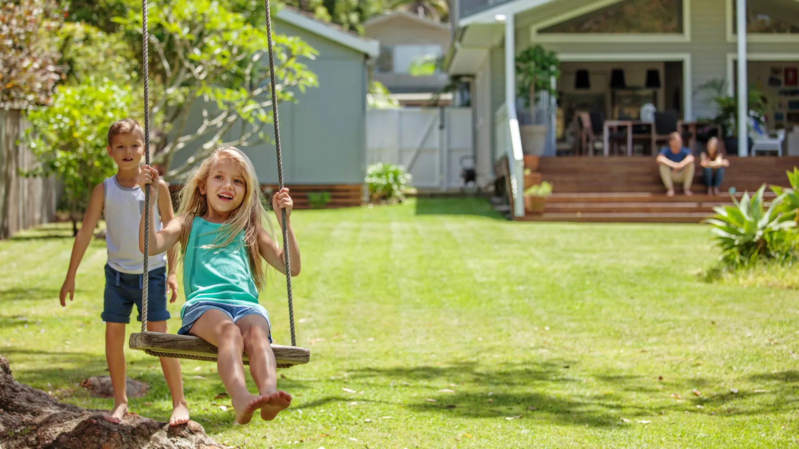boy pushing girl in swing in front of home