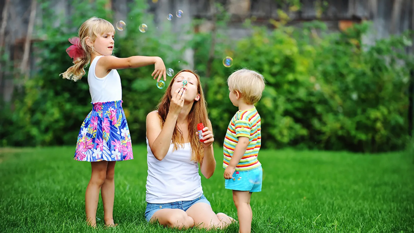 mom blowing bubbles in grass with kids