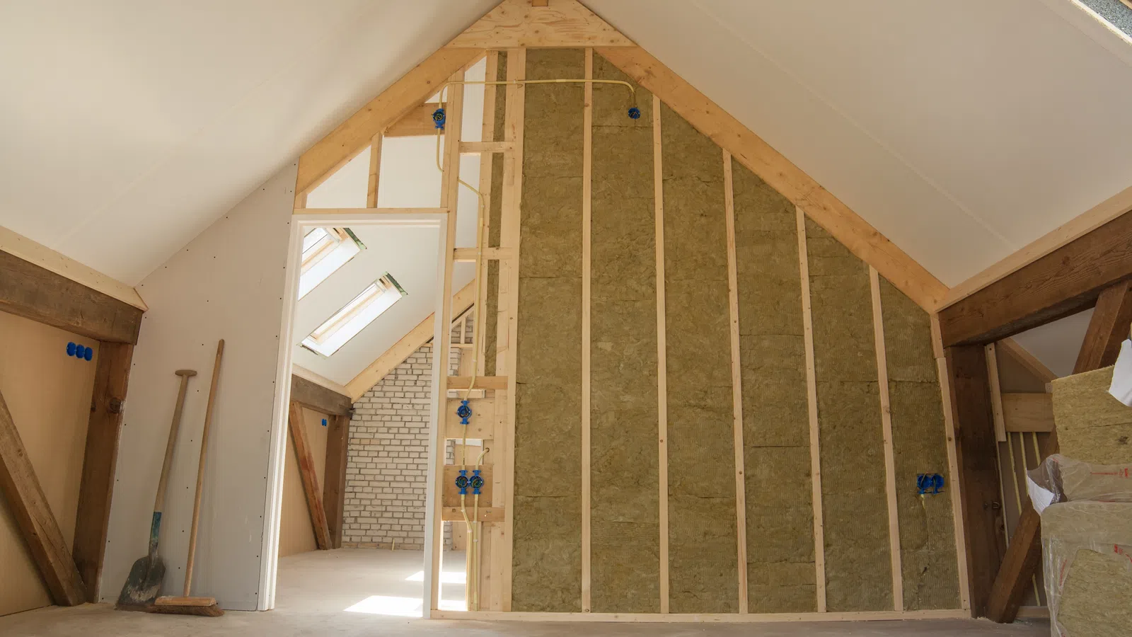 Interior attic space under construction with exposed insulation, wooden beams, and skylights.