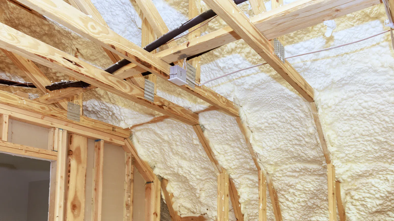 Wooden frame attic with white spray foam insulation applied between rafters and beams for energy efficiency.
