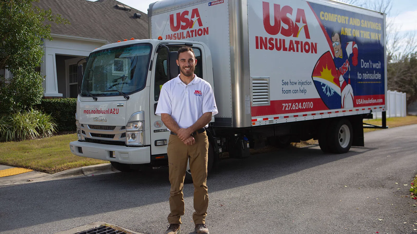 Man standing in front of USA Insulation truck parked on a suburban street near a house.