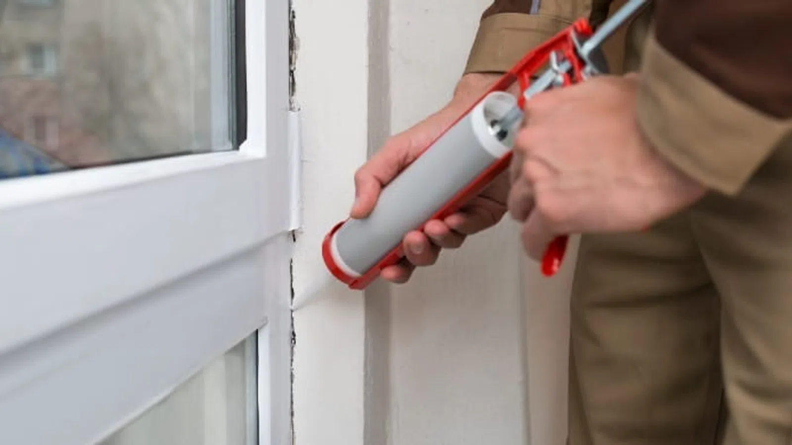 A person applying caulk to a window frame for sealing and insulation.