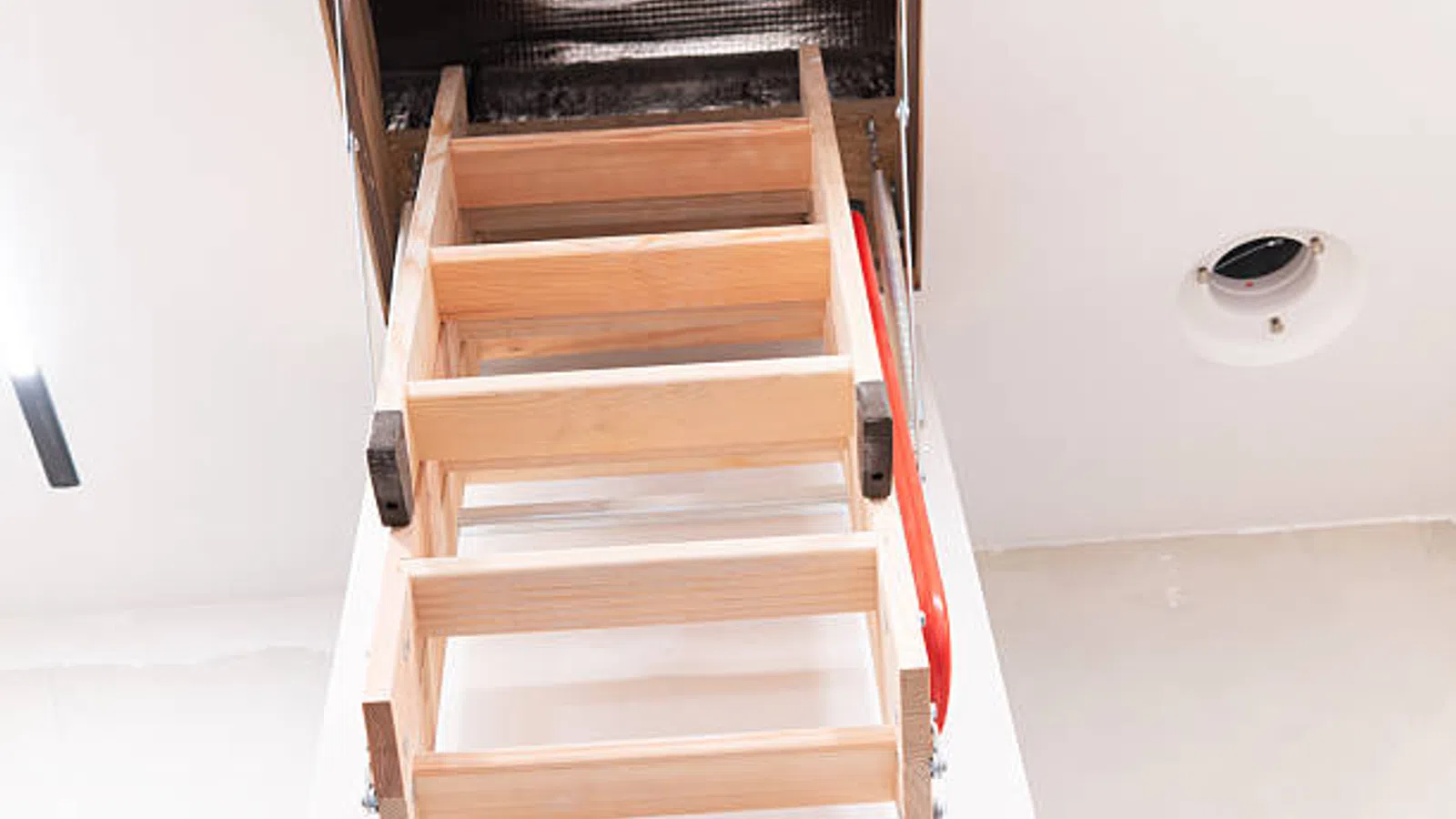 Pull-down wooden attic ladder extended from ceiling in a bright modern room.