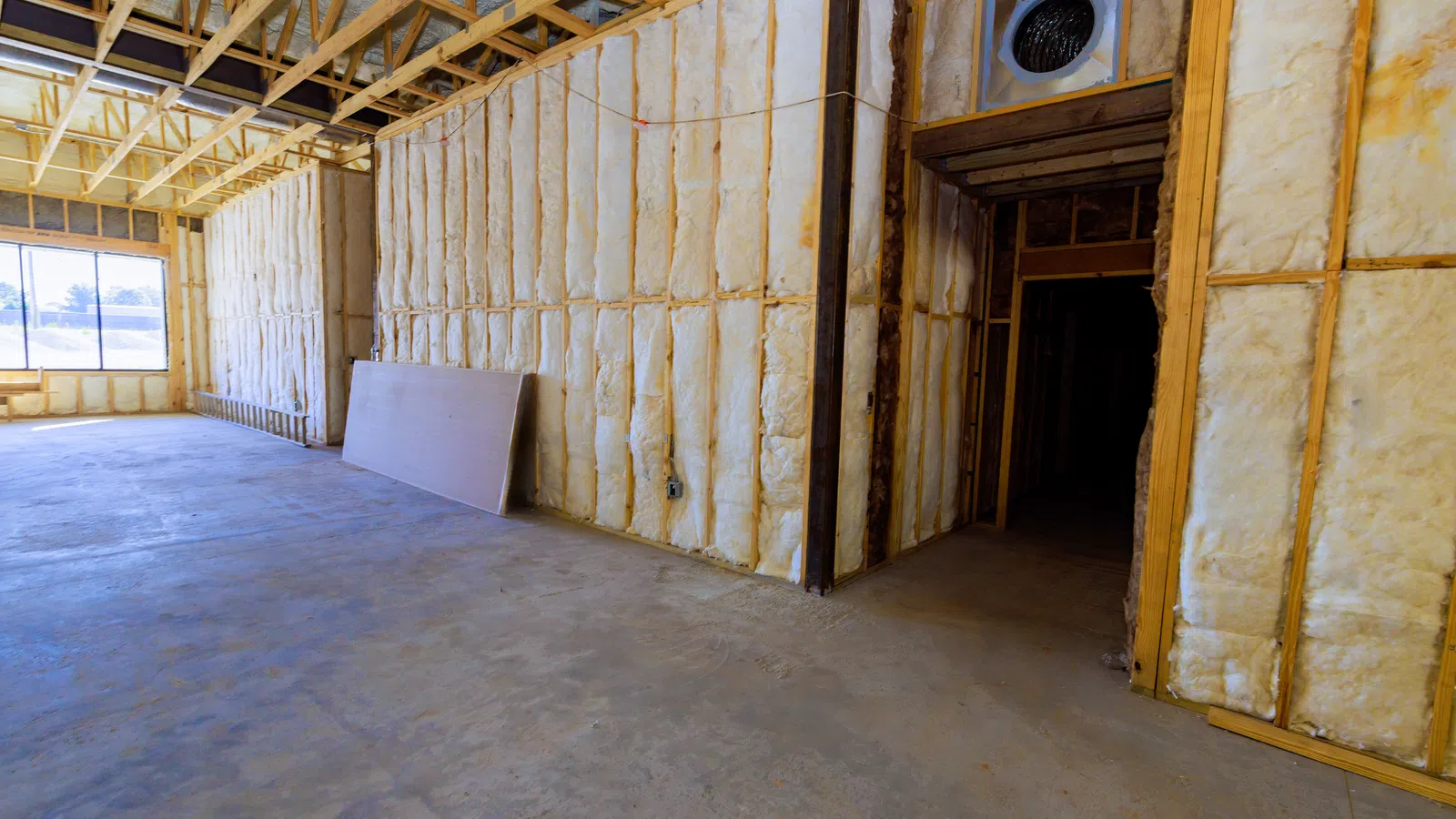 Interior of building under construction showing insulation installed between wooden framing and exposed ceiling beams.