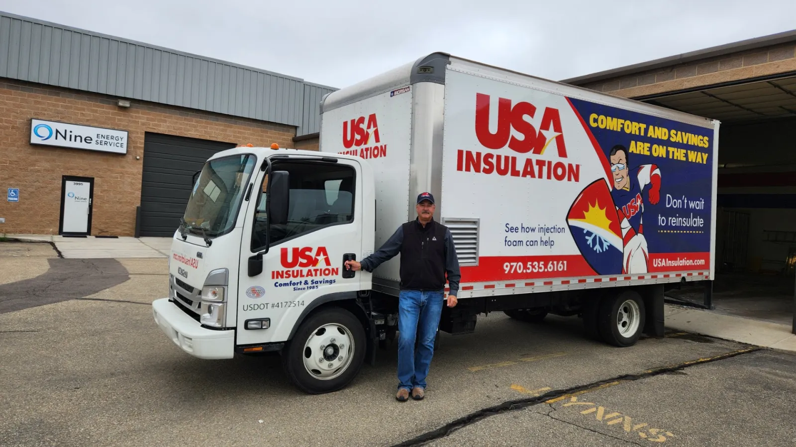 Man standing beside a USA Insulation truck with bold red and blue branding in a commercial parking lot.