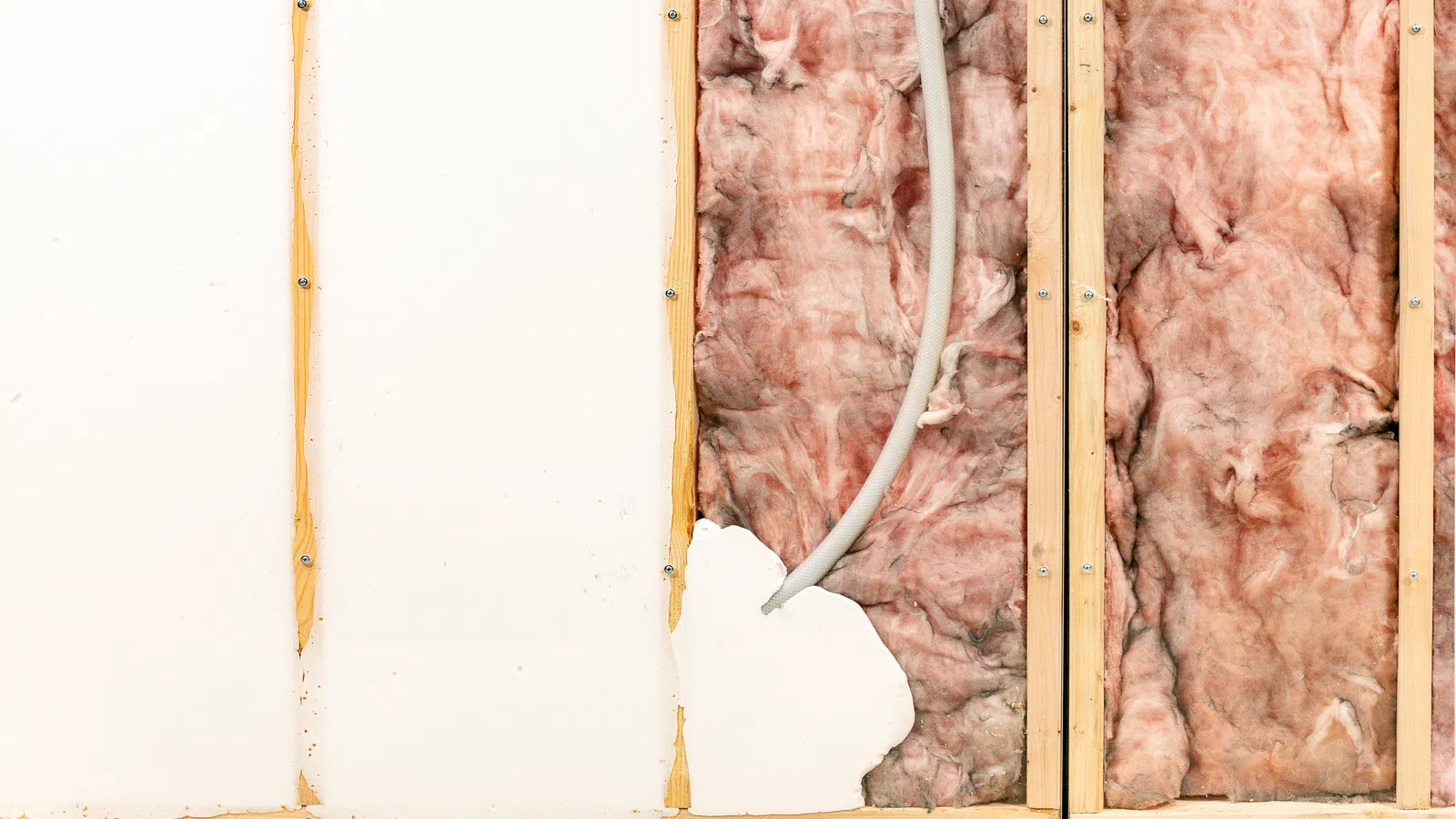 Wall partially stripped down exposing pink fiberglass insulation and electrical wiring in wooden framing.