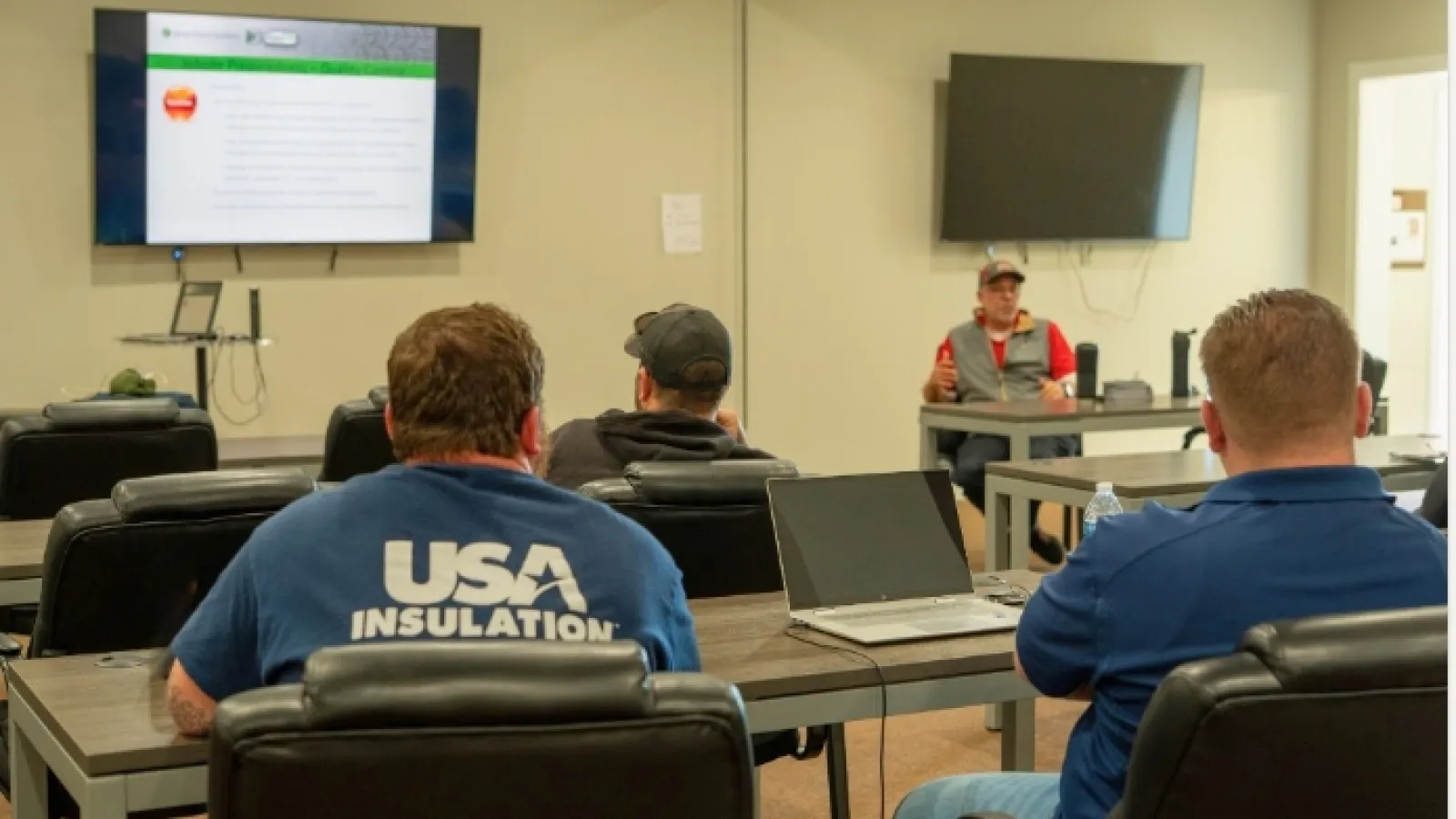 Workers attend a training session in a conference room with presentation slides and laptops visible.