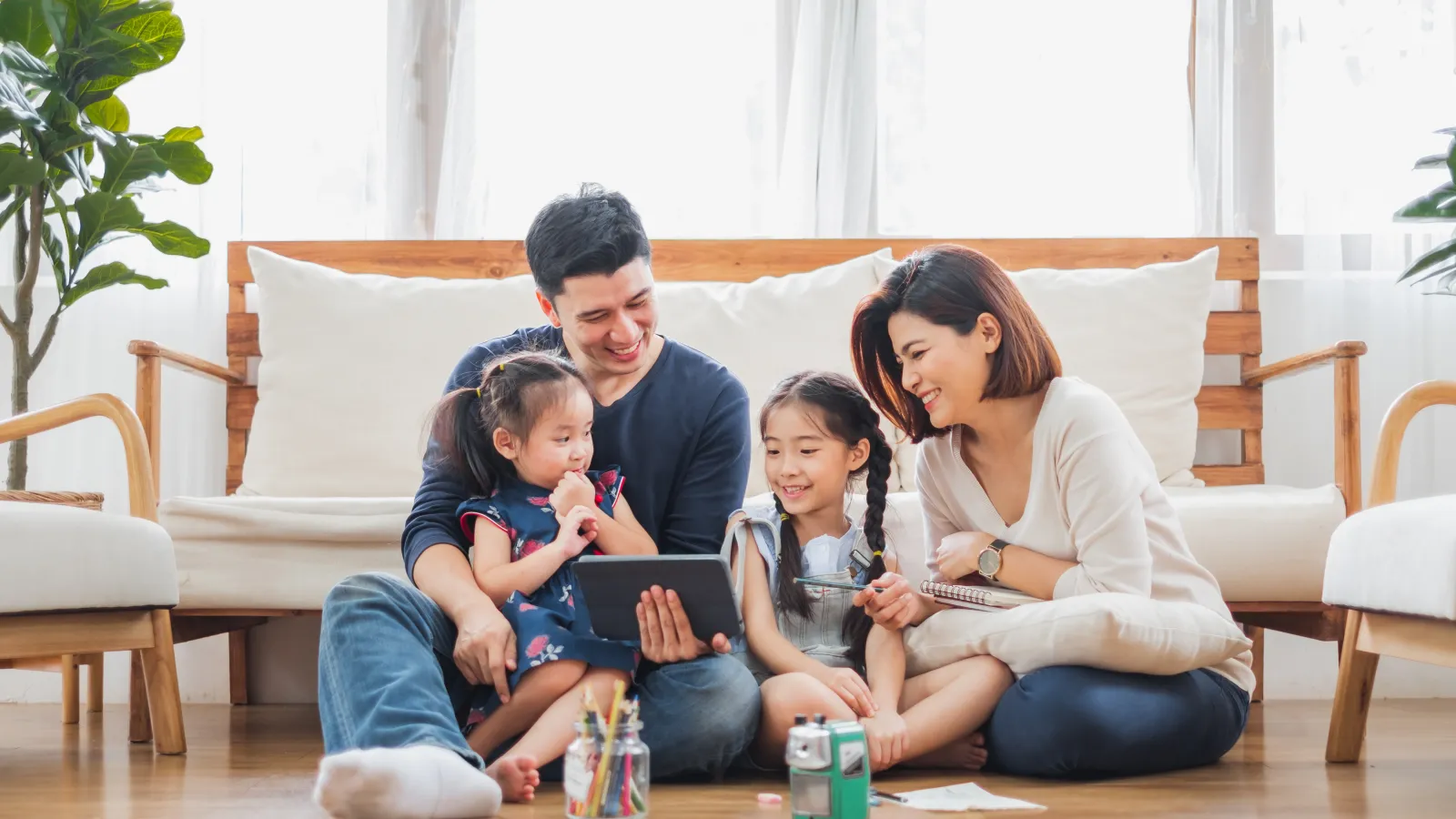 a man and a woman sitting on the ground holding a tablet with two little girls.