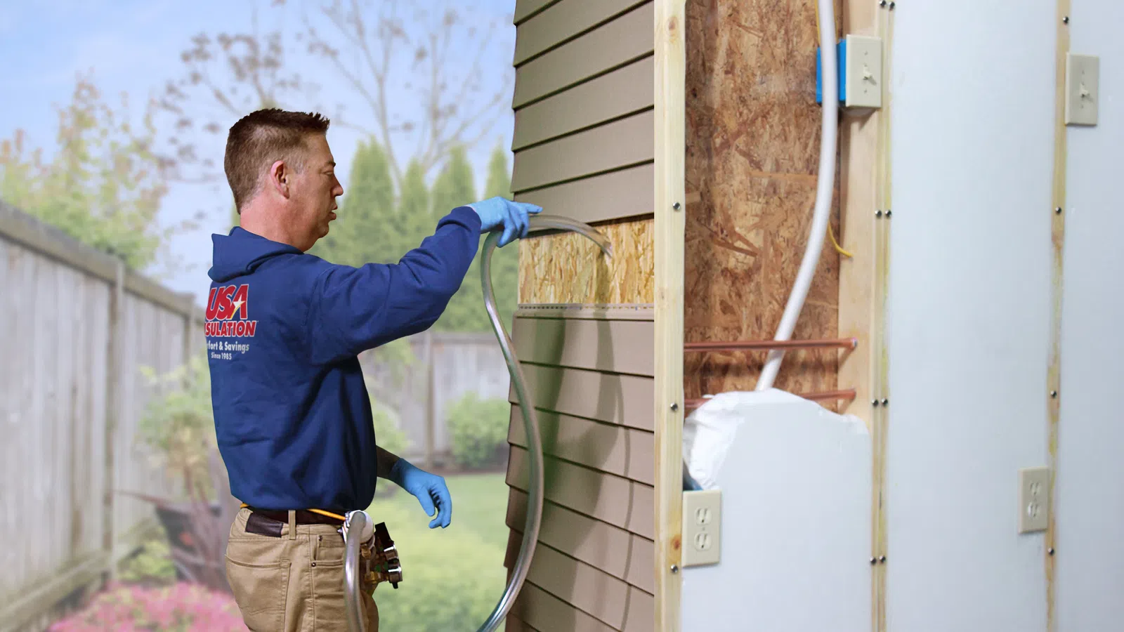 Worker installing rigid foam insulation on exterior wall of a house, wearing blue gloves and work gear outdoors.