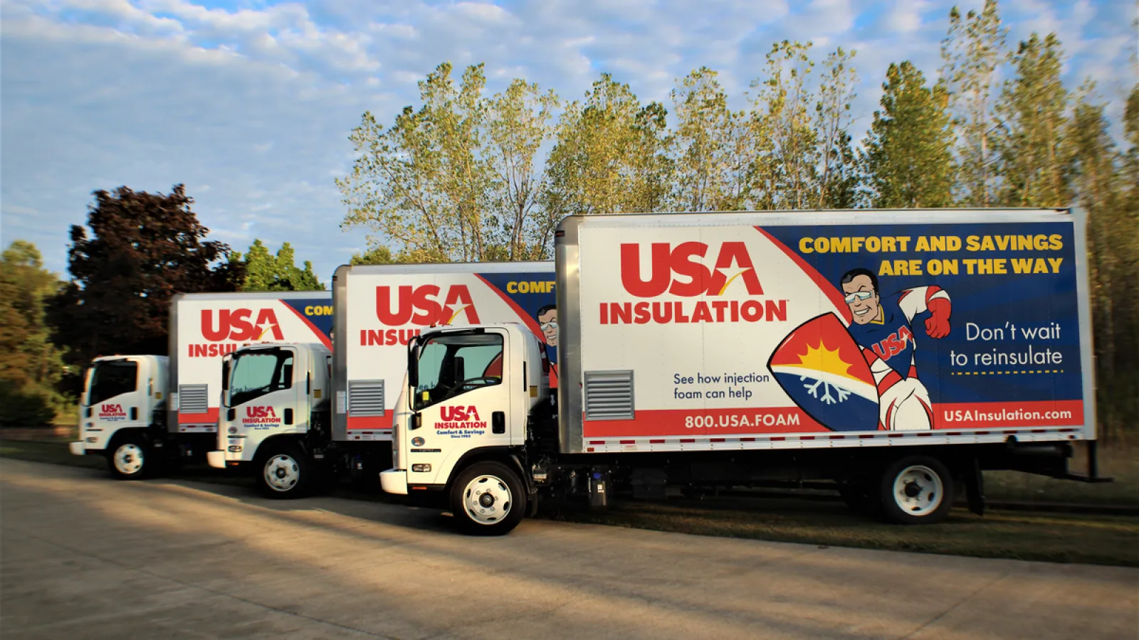 Three USA Insulation trucks parked in a row beside trees under a cloudy sky during daytime.