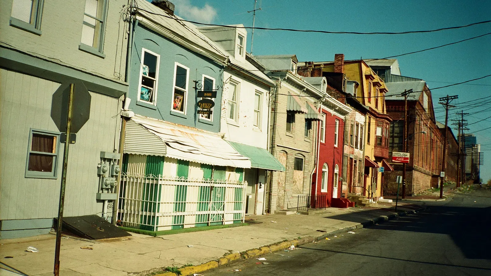 Quiet street with colorful old buildings, rusty awnings, and overhead power lines under clear blue sky.