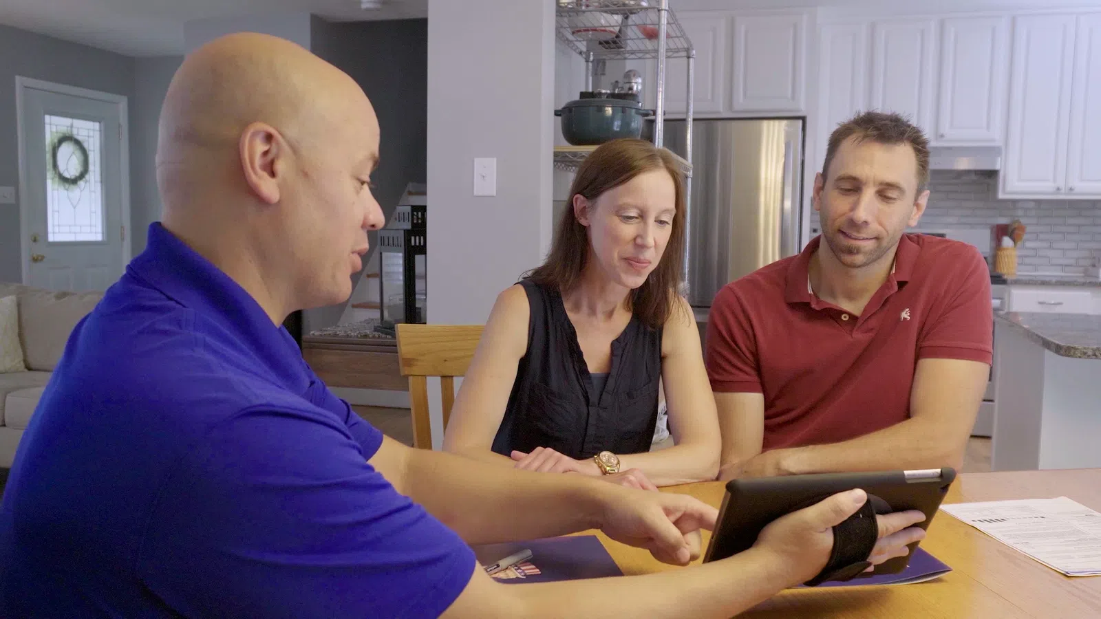 A consultant shows a couple an iPad while discussing plans at their kitchen table.