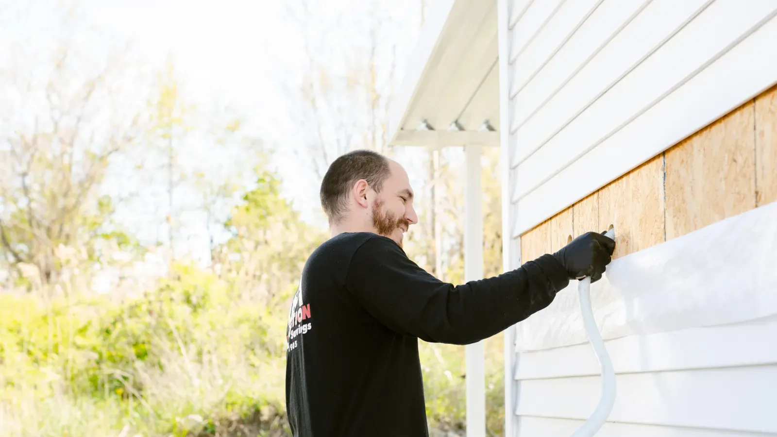 Man installing protective siding wrap on a house exterior wall on a sunny day