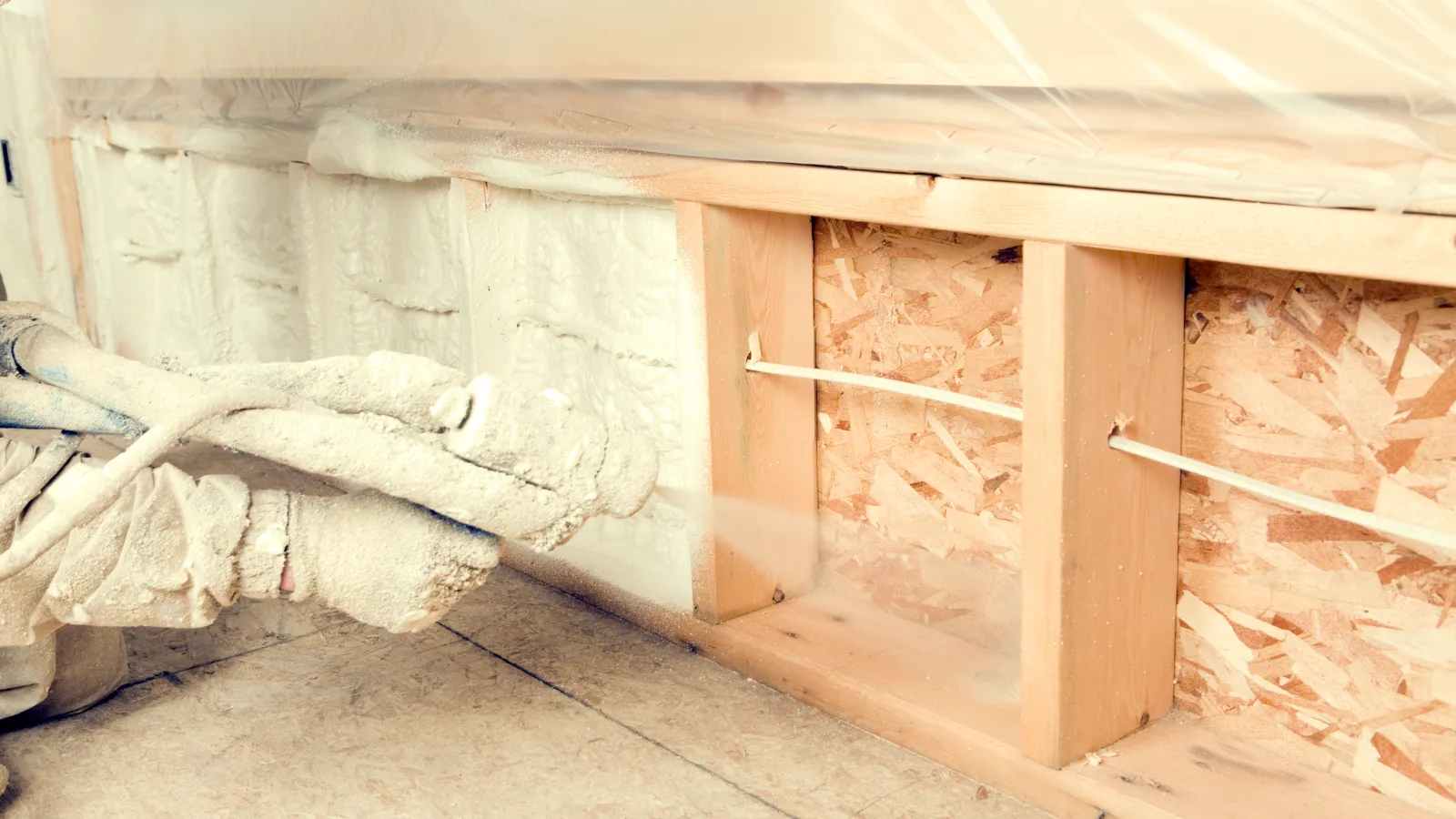 Close-up of spray foam insulation being applied to wooden wall framing for home energy efficiency.