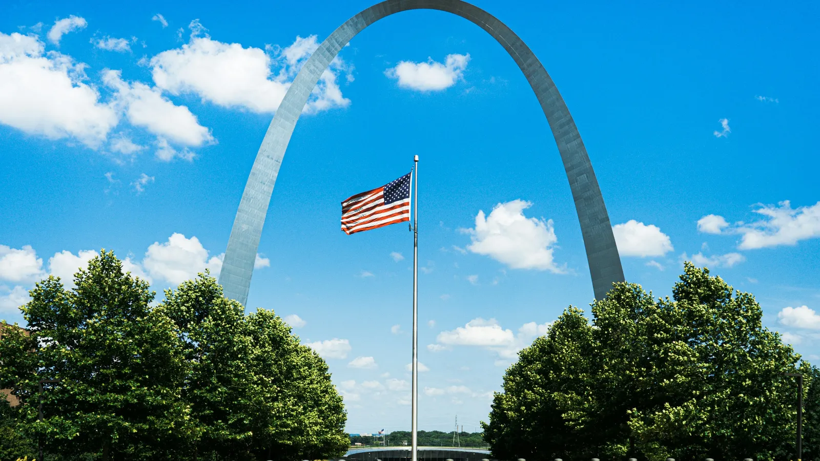 a flag on a flagpole with Gateway Arch in the background