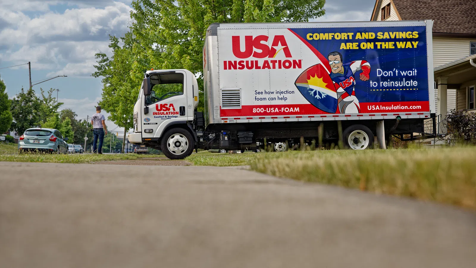 A USA Insulation truck parked on a suburban street with workers and green trees in the background.