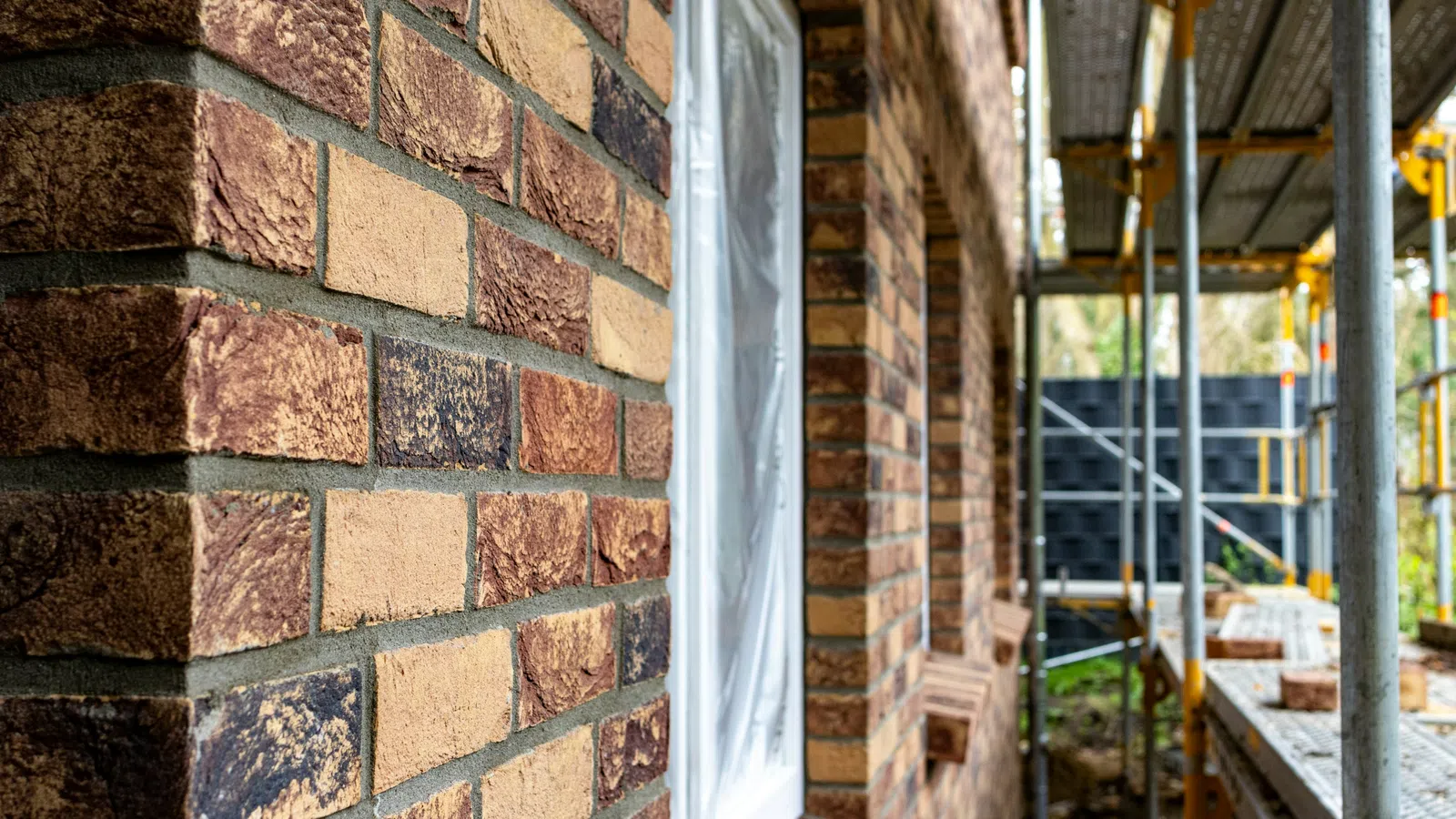 Close-up of a brick wall on a building under construction with scaffolding and a covered window.