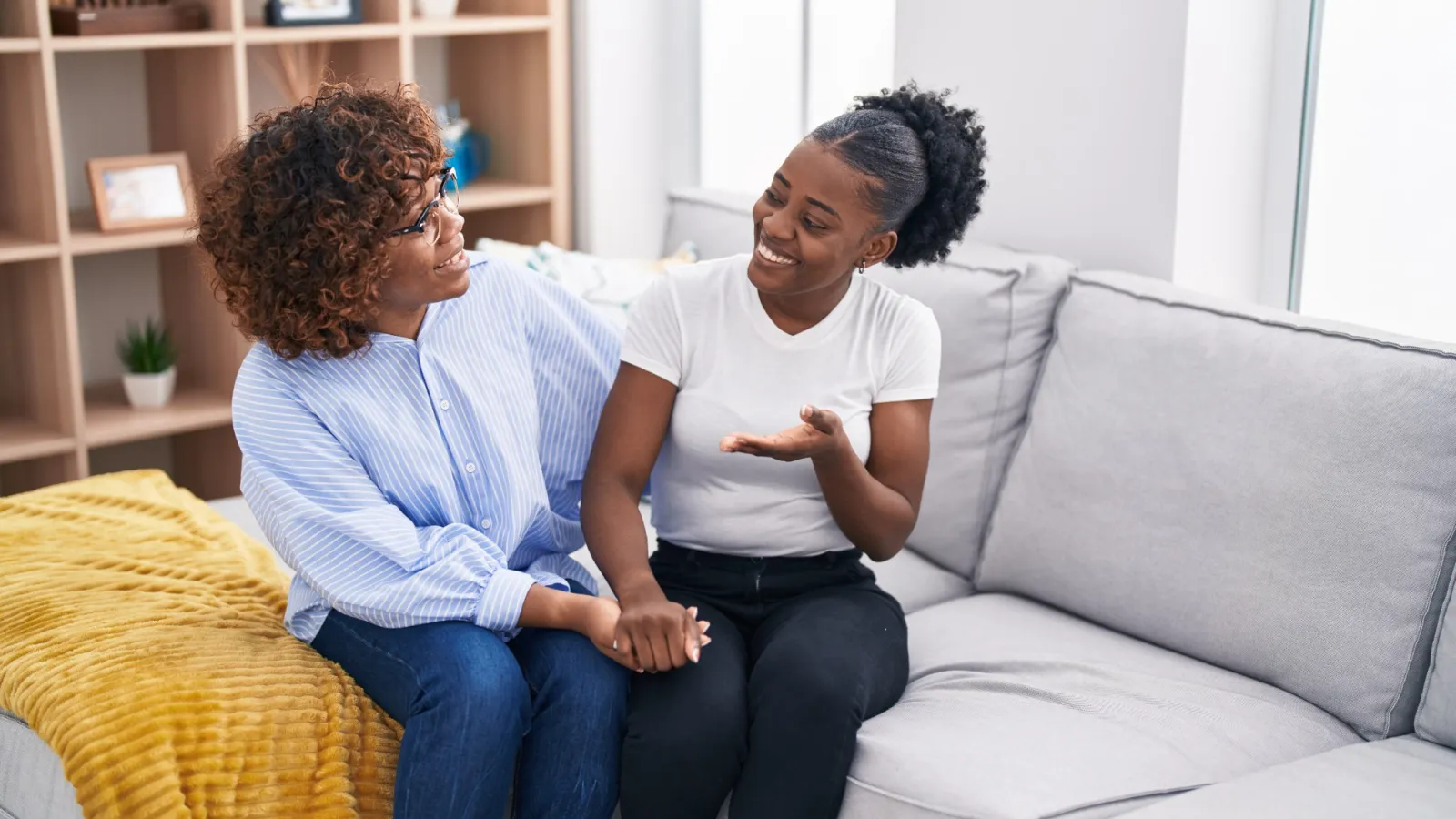 Two women sharing a joyful moment on a couch in a bright living room setting.