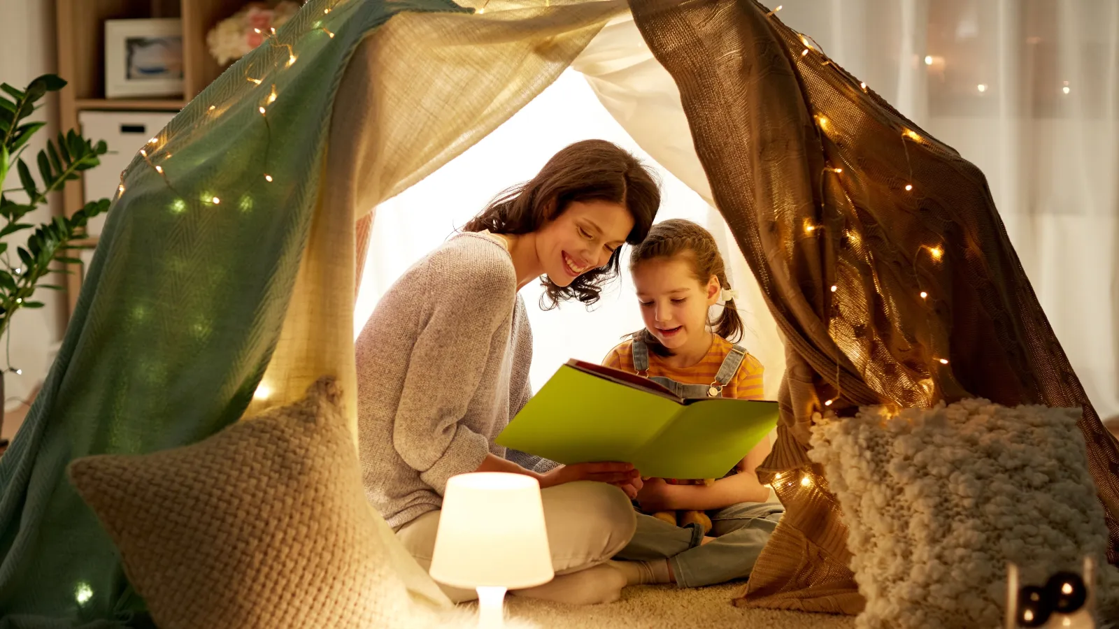 a person and a boy sitting in a tent reading a book