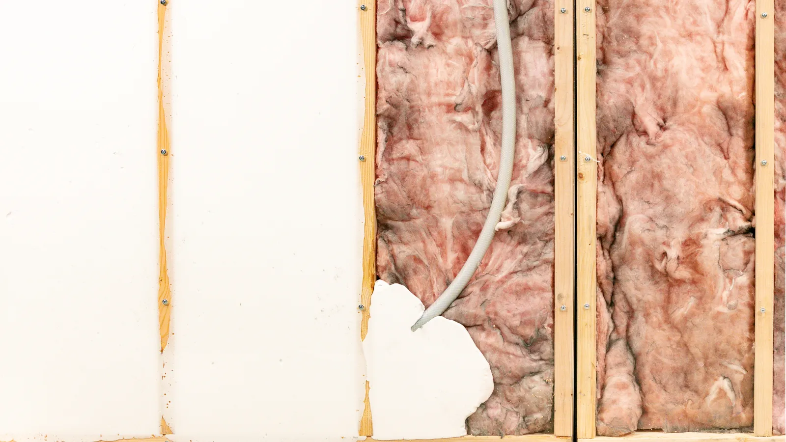Exposed house wall with pink fiberglass insulation and wooden studs behind torn drywall panel.
