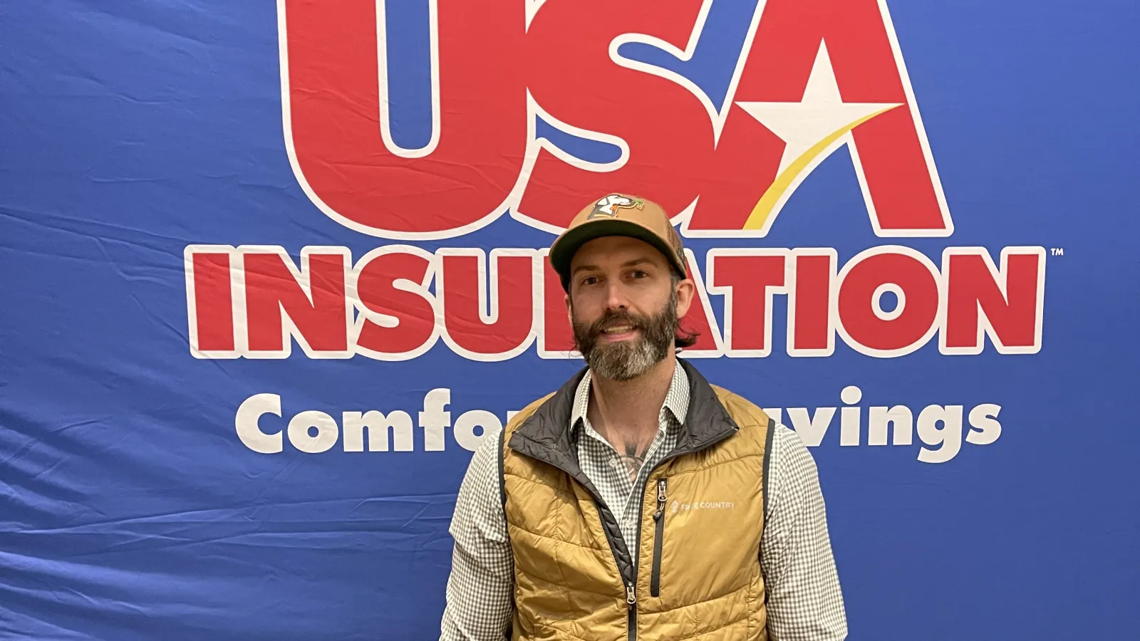 Man in a vest smiling in front of the USA Insulation logo backdrop.
