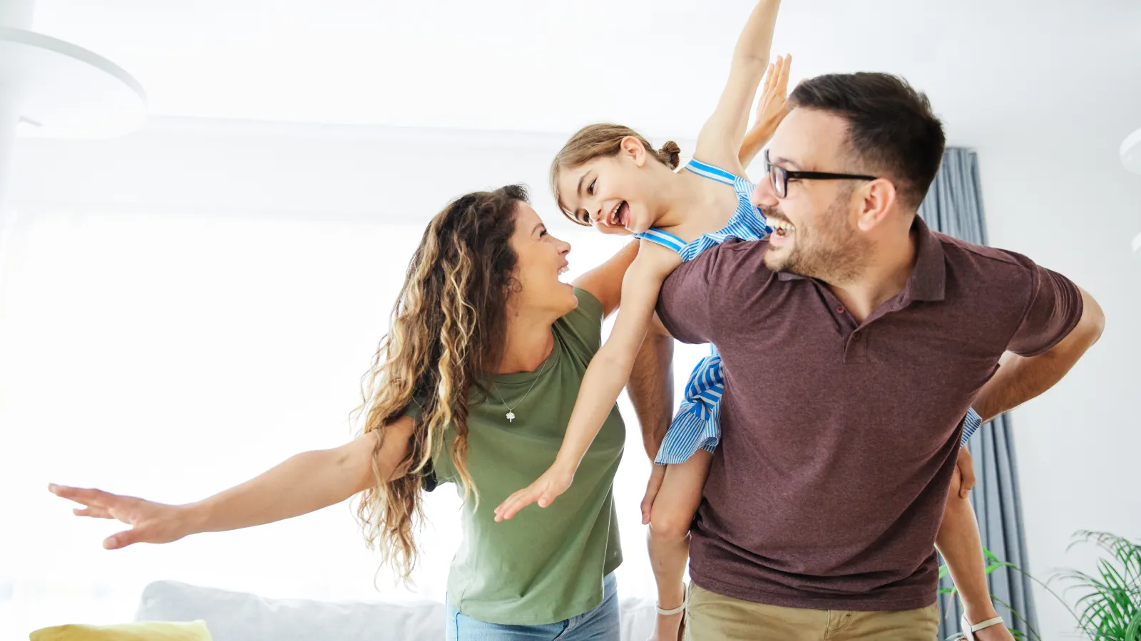 Happy family playing together at home, with a child on the father's back and parents smiling joyfully.