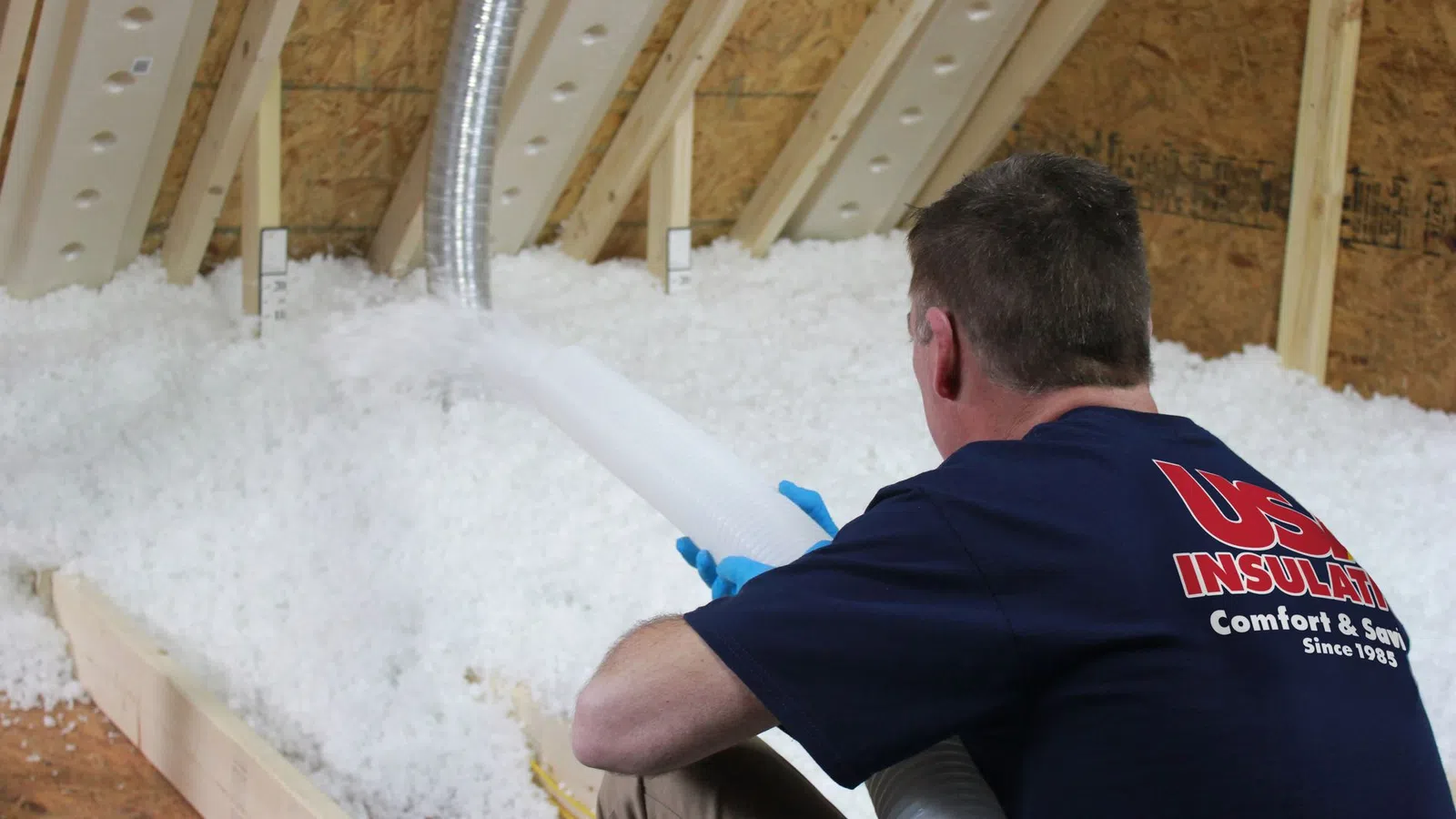 Technician blowing insulation into an attic filled with white insulating material.