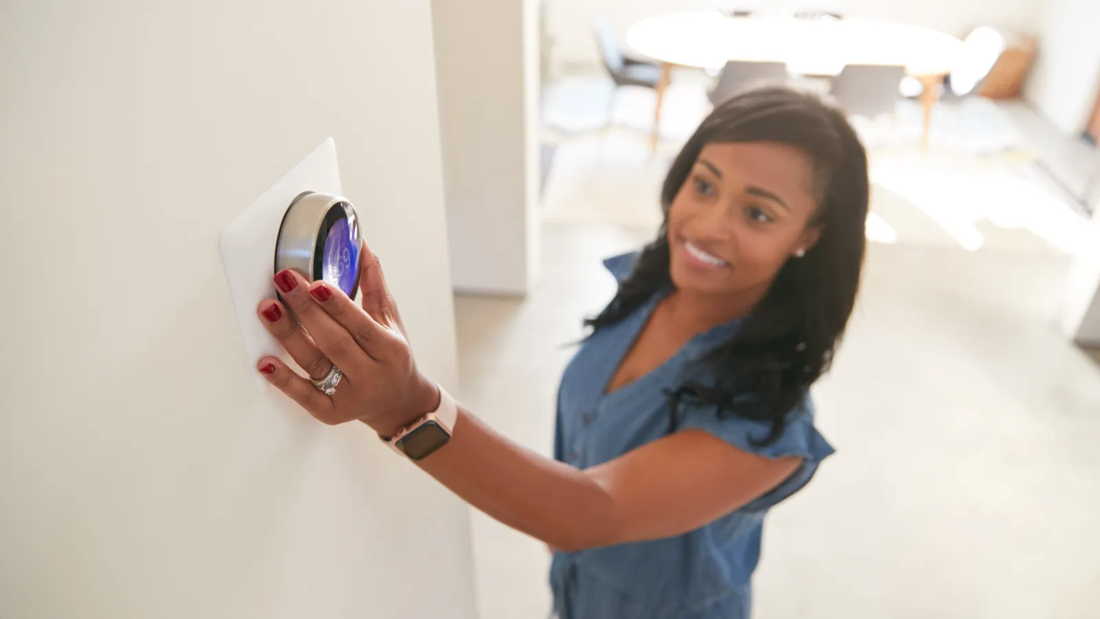 Woman adjusting a digital thermostat on a white wall in a bright modern home interior.