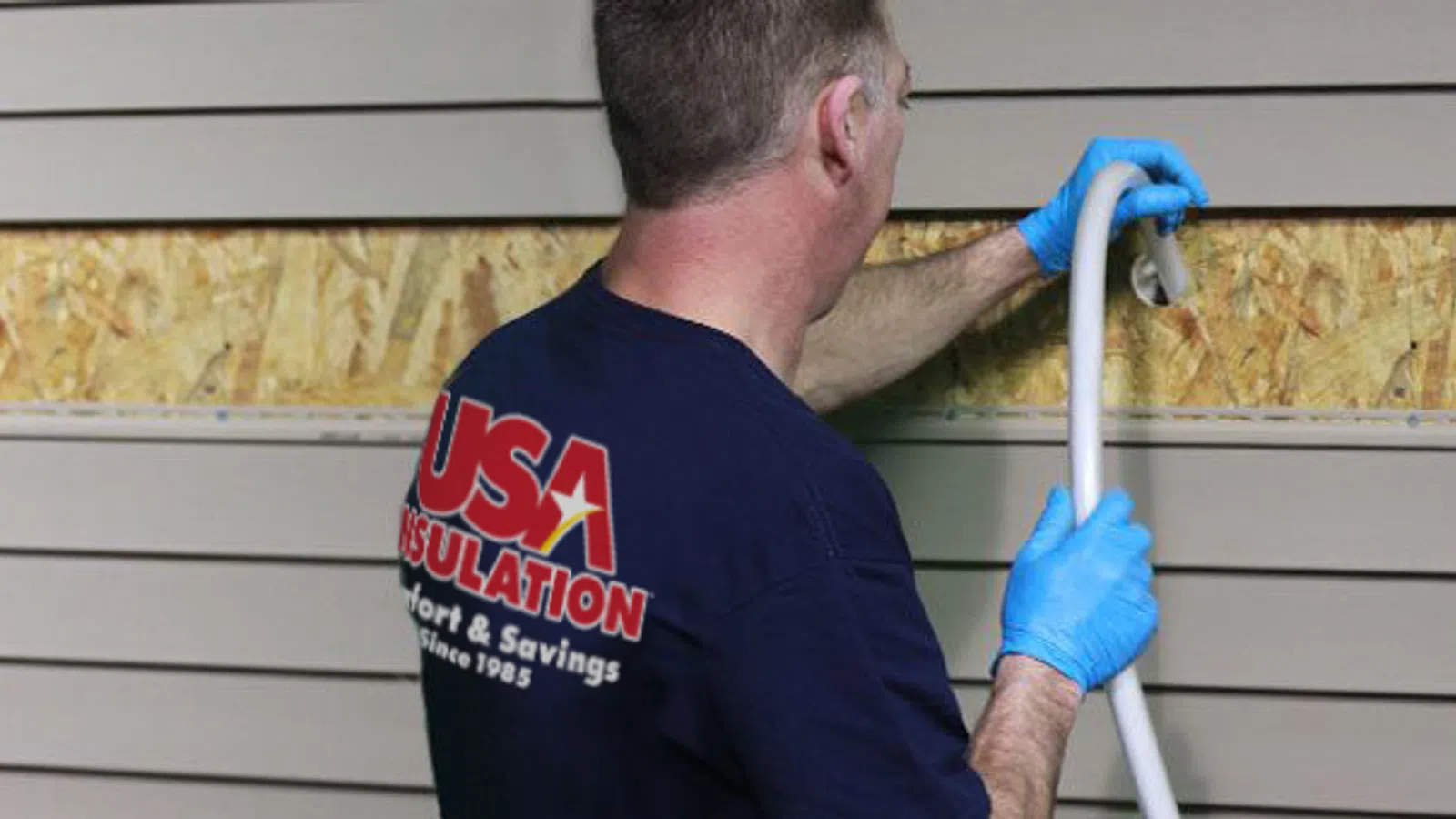 Worker installing foam insulation into wall panels wearing blue gloves and USA Insulation shirt
