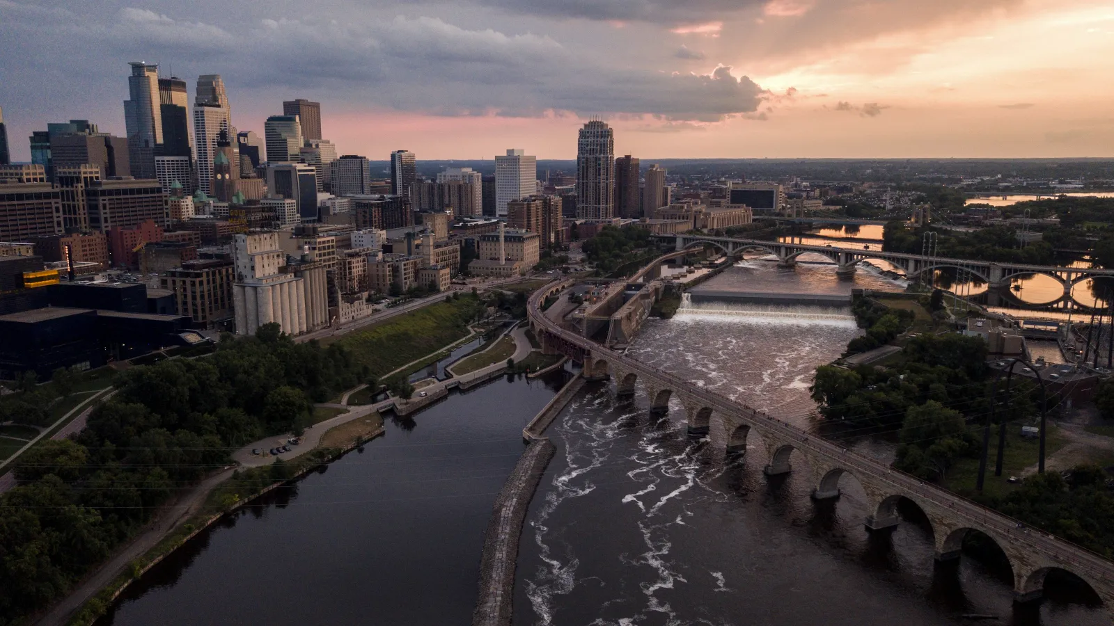 Aerial view of Minneapolis skyline at sunset with Mississippi River and historic stone arch bridge in foreground