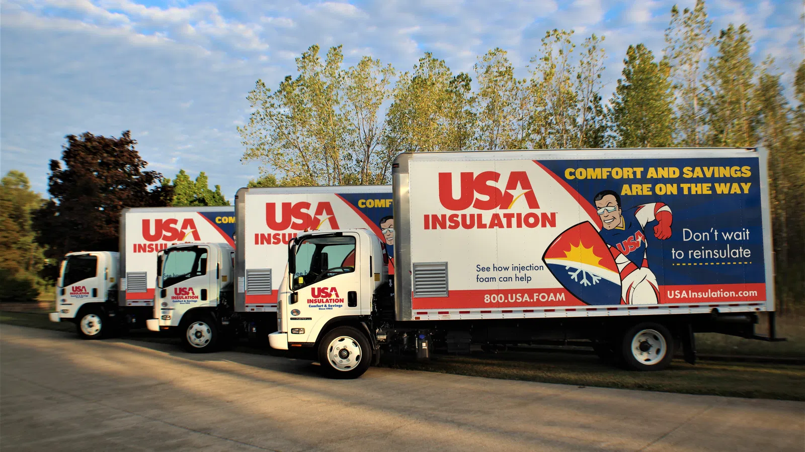 Three USA Insulation trucks parked in a row with promotional graphics about comfort and savings on insulation.