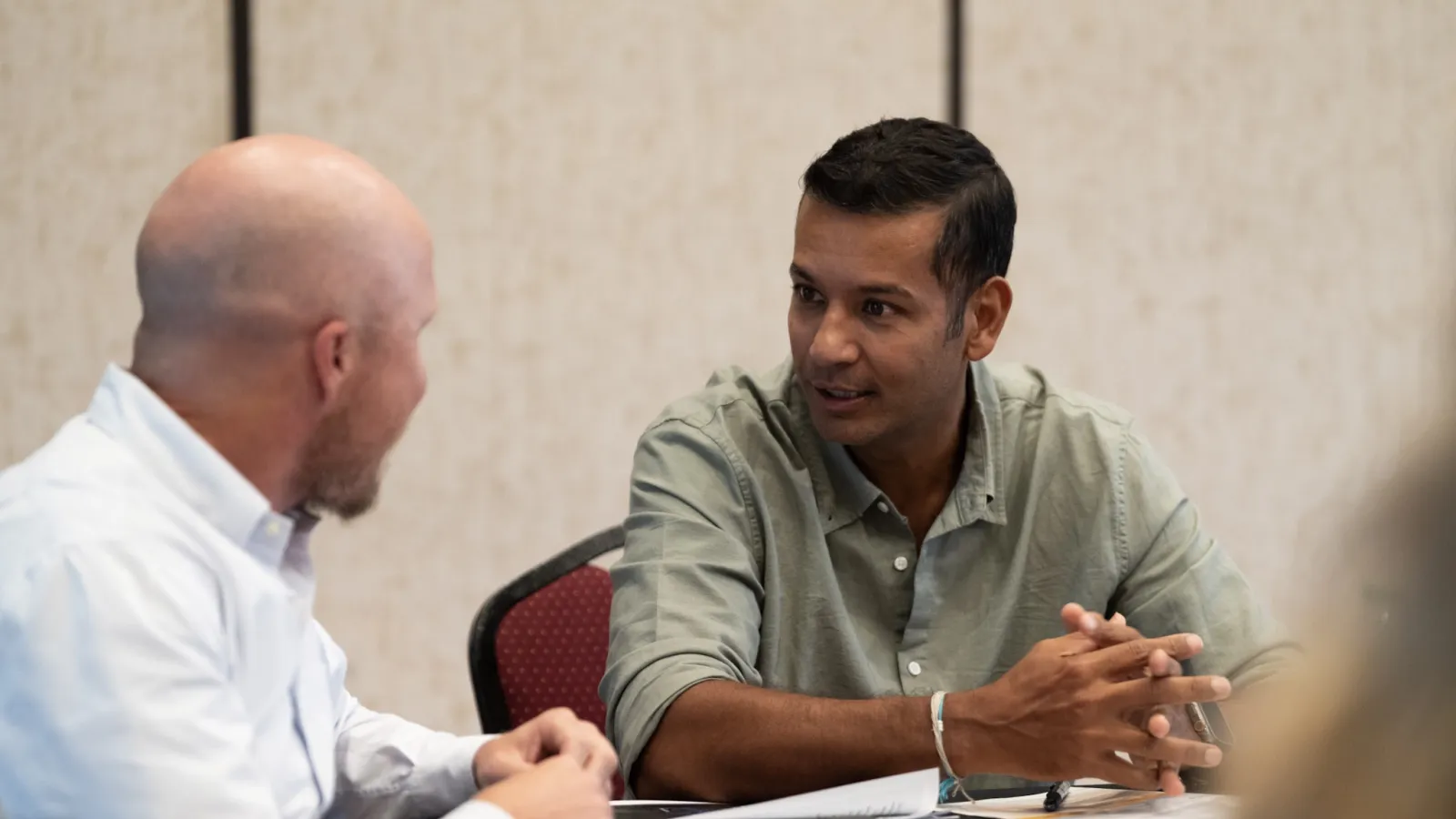Two men engaged in a focused discussion at a table with documents and a laptop in a professional setting