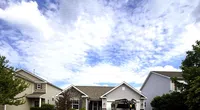 Suburban house with a truck in the driveway under a bright cloudy sky and Roof It Forward logo overlay.