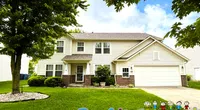 Two-story suburban house with white siding and brick facade under green trees on a sunny day