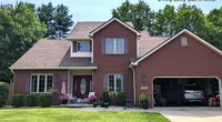 Two-story brick house with pitched roof, green lawn, American flag, and an open garage with a car inside