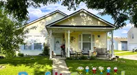 Yellow house with front porch and Roof It Forward painted on green lawn with cartoon children figures.